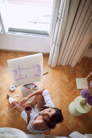 top view of a female painter holding glass of a red wine, looking up, in the camera.の写真素材