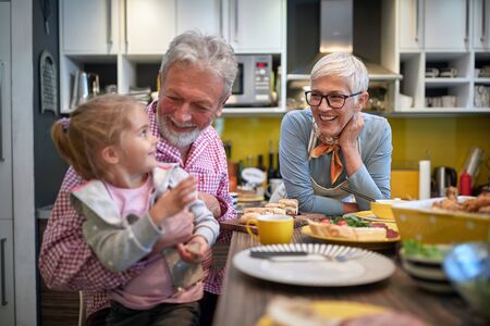 grandpa holding his granddaughter in a lap in a kitchen with grandma watching them