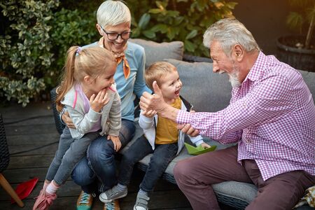 grandparents playing with their grandchildren on a sofa in the backyardの写真素材