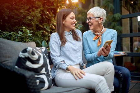 mother showing something on her cell phone to a daughter, smiling and laughing
