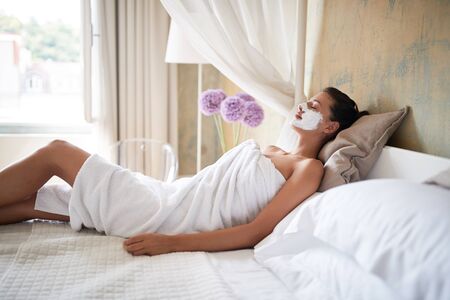 beautiful young woman relaxing at home with beauty mask on her faceの写真素材