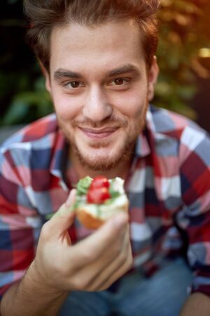 young male caucasian holding sandwich that is about to eat, looking at cameraの写真素材