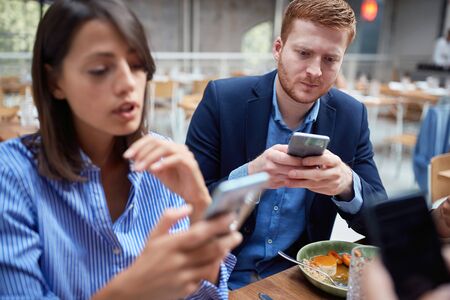 Young casual man and woman at business lunch texting message.の写真素材