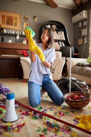 tired young woman cleaning the house after a kid birthday partyの写真素材
