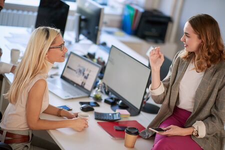 Two female colleagues chatting in the office, business hub concept
