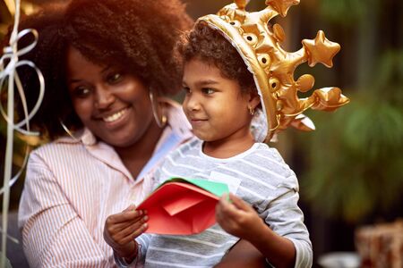 Afro american cute little girl with crown at head playing with paper boats.の写真素材