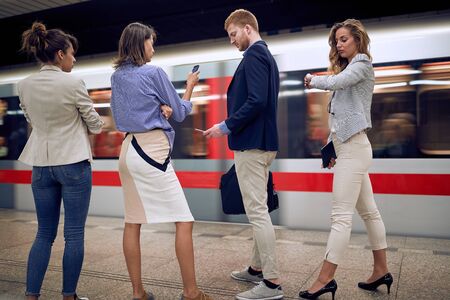 group of young businesspeople watching at their cell phones, wrist watch, in a subway. time goes by quickly conceptの写真素材