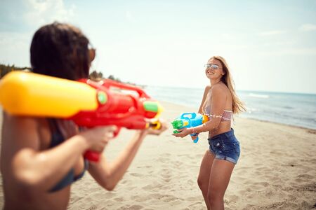 Young friends having fun on the beach.Playful girl have fun with water gun at beach at sunny day.の写真素材