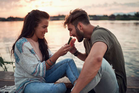 young woman feeding man with slice of watermelon by the sea