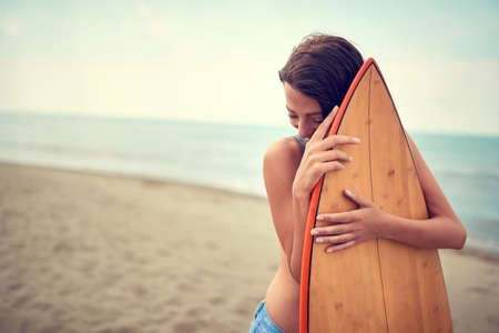 A young female surfer posing with her board on a beachの写真素材
