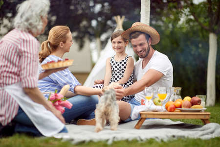 happy little caucasian girl sitting in dad's lap, surrounded by family at picnic. love and affection, joy conceptの写真素材