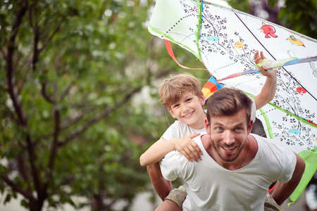 young dad running with son on his back with kite in his hand, having funの写真素材