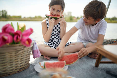 cute girl and boy eating watermelon at picnic by the river. cuteness overloadの写真素材