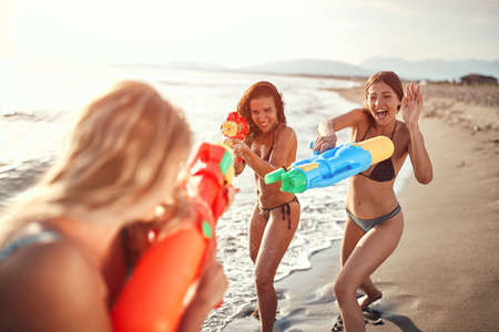 three women spray each other with water from water guns on a sandy beachの写真素材