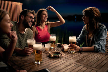 Smiling friends talking and drinking beer and enjoying a beautiful evening.の写真素材