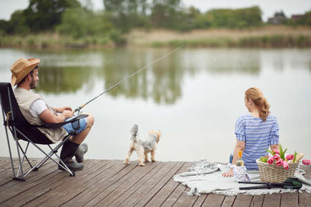 Spouses enjoy fishing and a picnic with their dog on a beautiful dayの写真素材