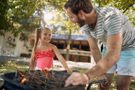 Father with his smiling daughter prepare fire for family  barbeque.の写真素材