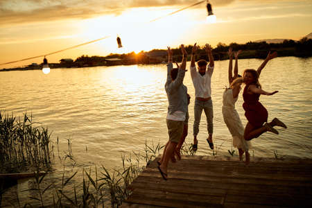 Group of friends jumping on the shore of the lake on the sunset