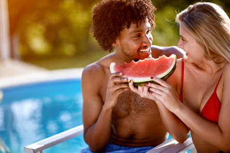 Man and woman relaxing near swimming pool.Smiling couple eating watermelon together.の写真素材