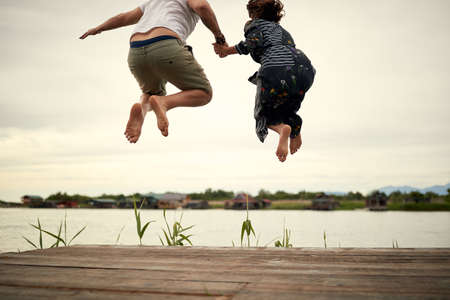 Young couple in love jumping on the shore of the lake on a beautiful weatherの写真素材