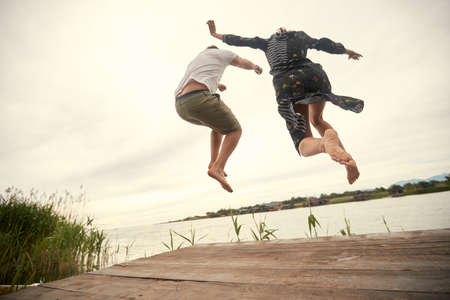 Young couple jumping on the shore of the lake on a beautiful weatherの写真素材