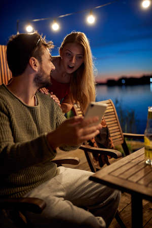 young guy showing content on his cell phone to a female friend at nightの写真素材