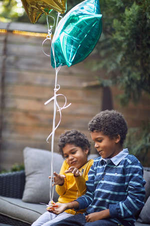 afro-american boy and girl playing, holding balloons, sitting outdoorの写真素材