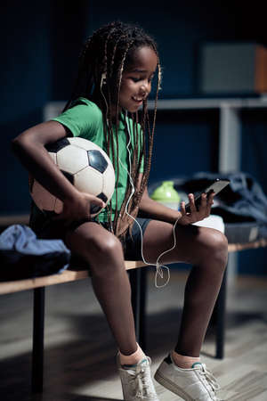 A little soccer player enjoying content on cell phone waiting for a training  in a locker roomの写真素材