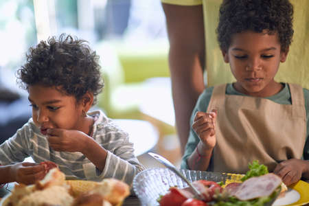 afro-american little girl and boy eating together with their fingersの写真素材