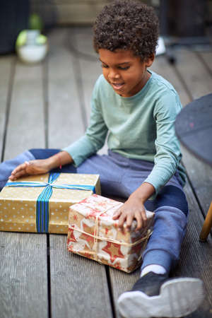 little afro-american boy sitting on the floor, looking presents that he got for a birthdayの写真素材