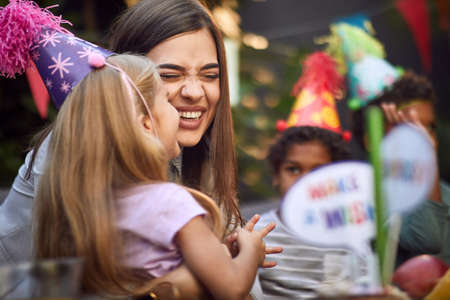 cute little blonde girl kissing young adult female at birthday partyの写真素材