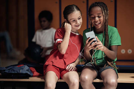 The little soccer teammates enjoying content on cell phone waiting for a training in a locker roomの写真素材