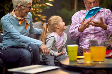 grandfather amusing his granddaughter, throwing up and down blue paper boat, laughing