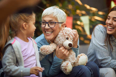 grandmother holding teddy bear, playing with her granddaughter, smiling