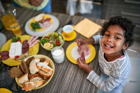 Top view of cheerful female child while eating in kitchenの写真素材