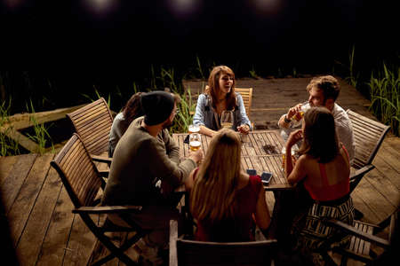 Group of cheerful friends enjoying a drink in the bar on the lake with a beautiful nightの写真素材