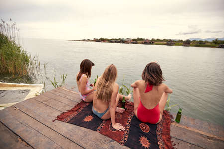 Young attractive girls in bikini with the beer taking a rest on the shore of the lake on a sunny weatherの写真素材
