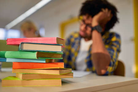A lot of books in front of male student at the university classroom