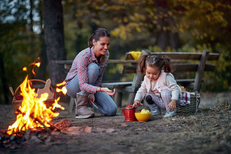 Mother and daughter playing around a campfire in the forest on a beautiful autumn duskの写真素材