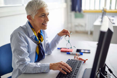 A female professor typing on a computer at a lecture in the university classroom. Professor working at the college. Education, college, university, learning and people conceptの写真素材