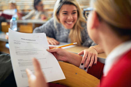 Female student in university amphitheater happy about high grade at the exam. Smart young people study at the college. Education, college, university, learning and people conceptの写真素材