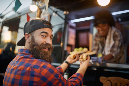 happy, satisfied caucasian male with beard customer receiving sandwiches from a polite employee in...