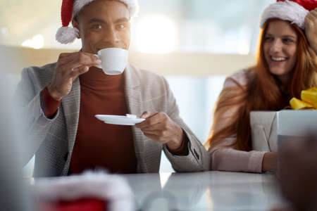young afro-american employee drinking coffee in the office, wearing plaid jacket, turtleneck sweater...
