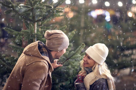 A young cheerful couple enjoying buying a christmas tree in a magical night of a snowy weather in the city. Christmas tree, love, relationship, Xmas, snowの写真素材