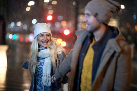 A young couple having good time together in a magical night on a snowy weather in the city. Love,...