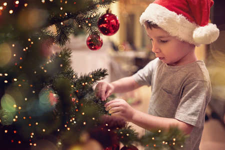 A little kid ornamenting a Christmas tree in a holiday atmosphere at home. Together, New Year, family, celebrationの写真素材