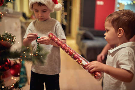 Children playing while decorating a Christmas tree in a holiday atmosphere at home together....