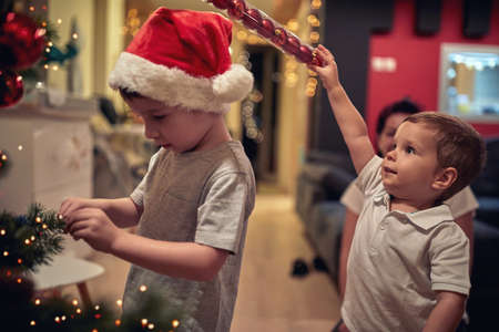 Children having fun decorating a Christmas tree in a holiday atmosphere at home. Together, New Year, family, celebrationの写真素材