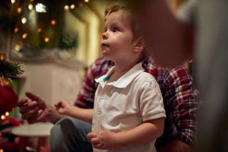 cute little caucasian kid looking at christmas tree with a dad behind himの写真素材