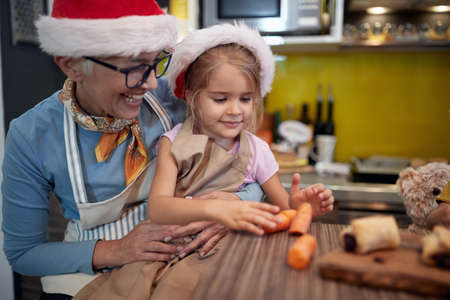 Grandma and granddaughter preparing Xmas meal in the kitchen in cheerful atmosphere together. Christmas, family, togetherの写真素材